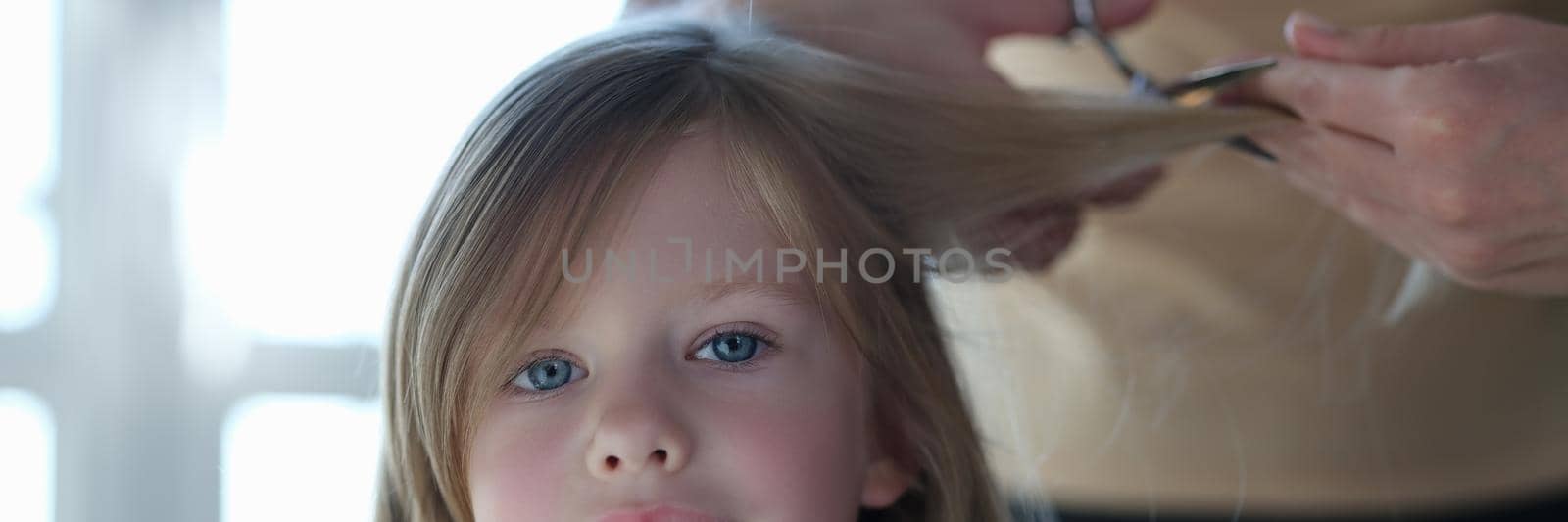 Woman scissors hair of cute blonde little girl closeup by kuprevich