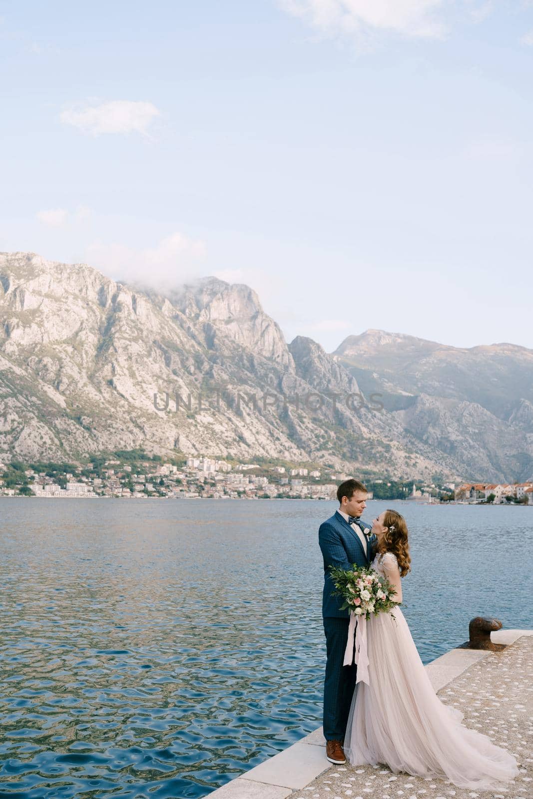 Groom hugs bride on the pier against the background of mountains. High quality photo