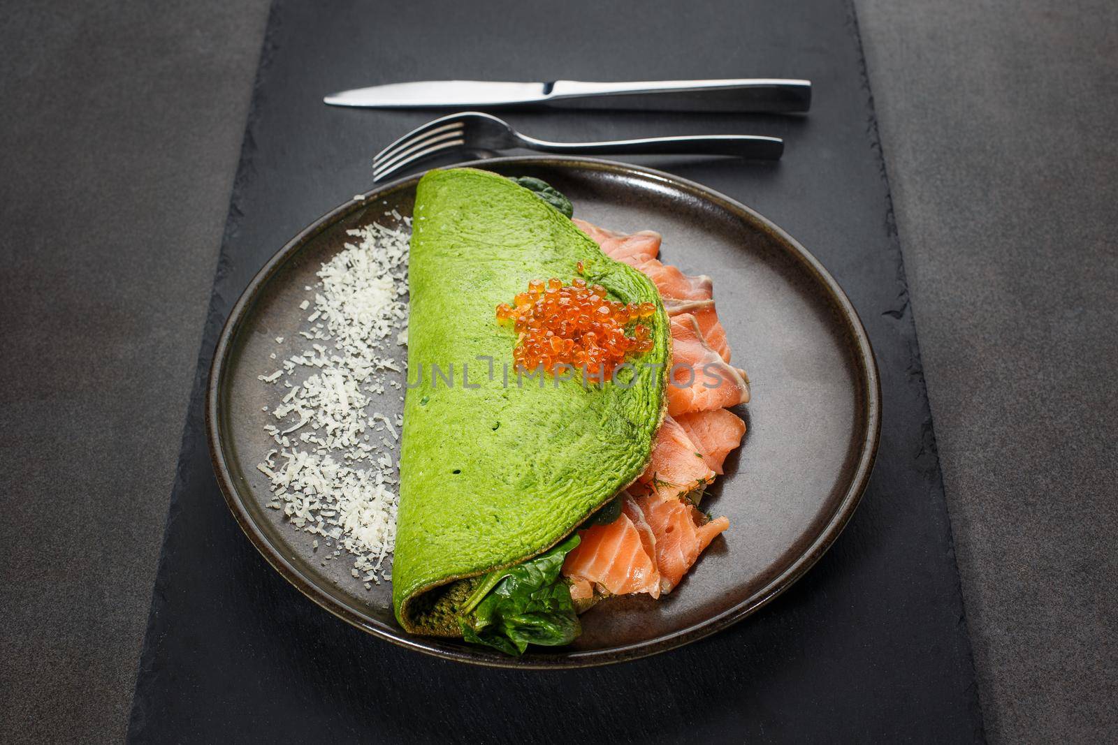 Green spinach omelet with samon and caviar on a dark plate. front view, dark background.