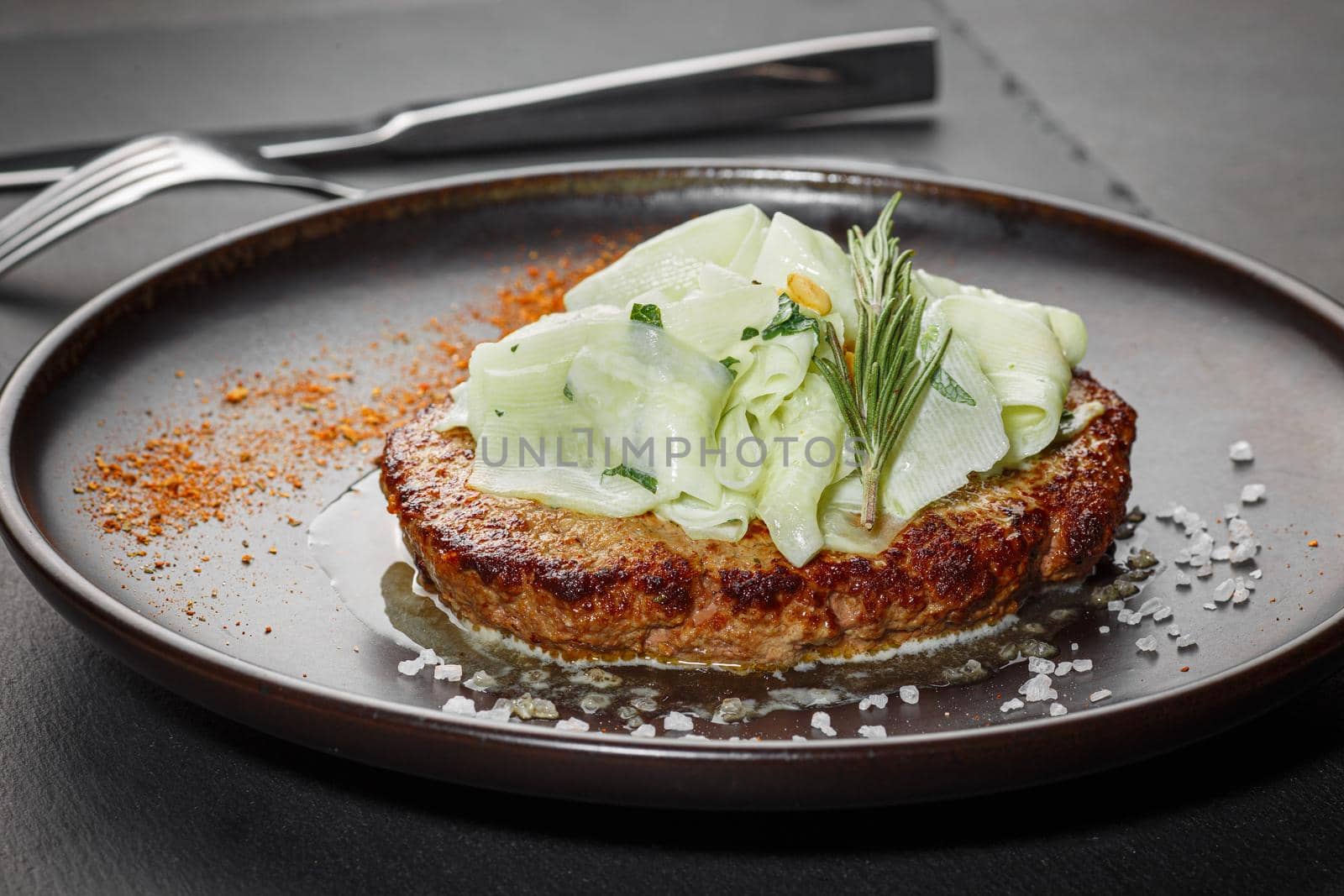 Roasted cutlet from beef and pork meat with zucchini slices and pine nuts. Black background. Front view