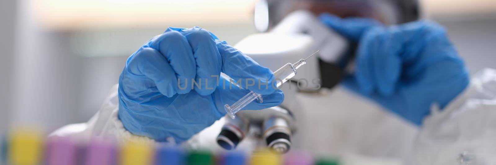 Scientist looks through microscope at glass syringe witha needle. Development of new vaccines concept