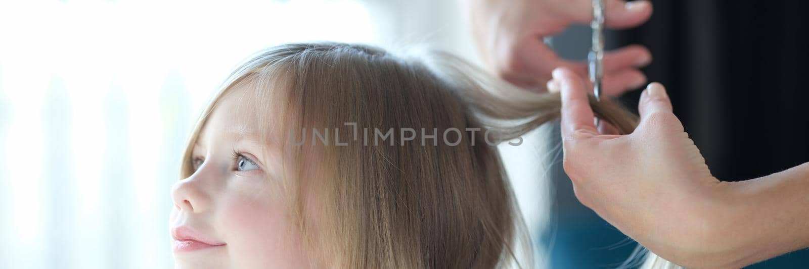 Beautiful little girl hairdresser cuts hair. Haircut for children at home concept