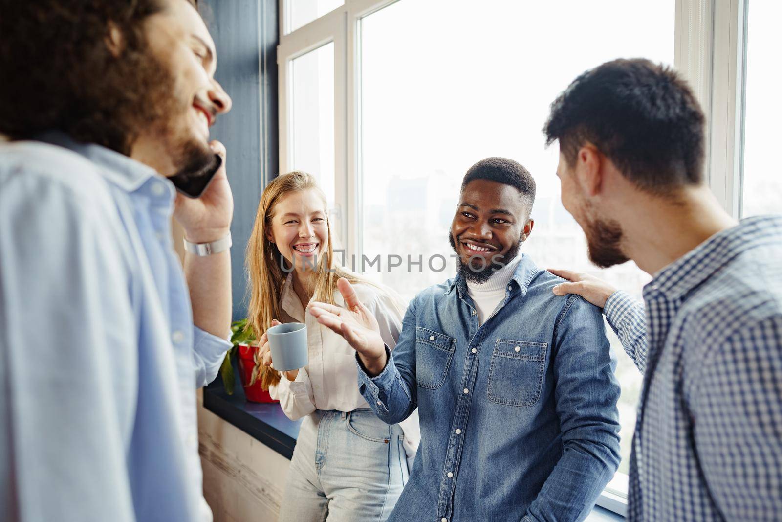 Cheerful young business people have a talk during coffee break in office near window