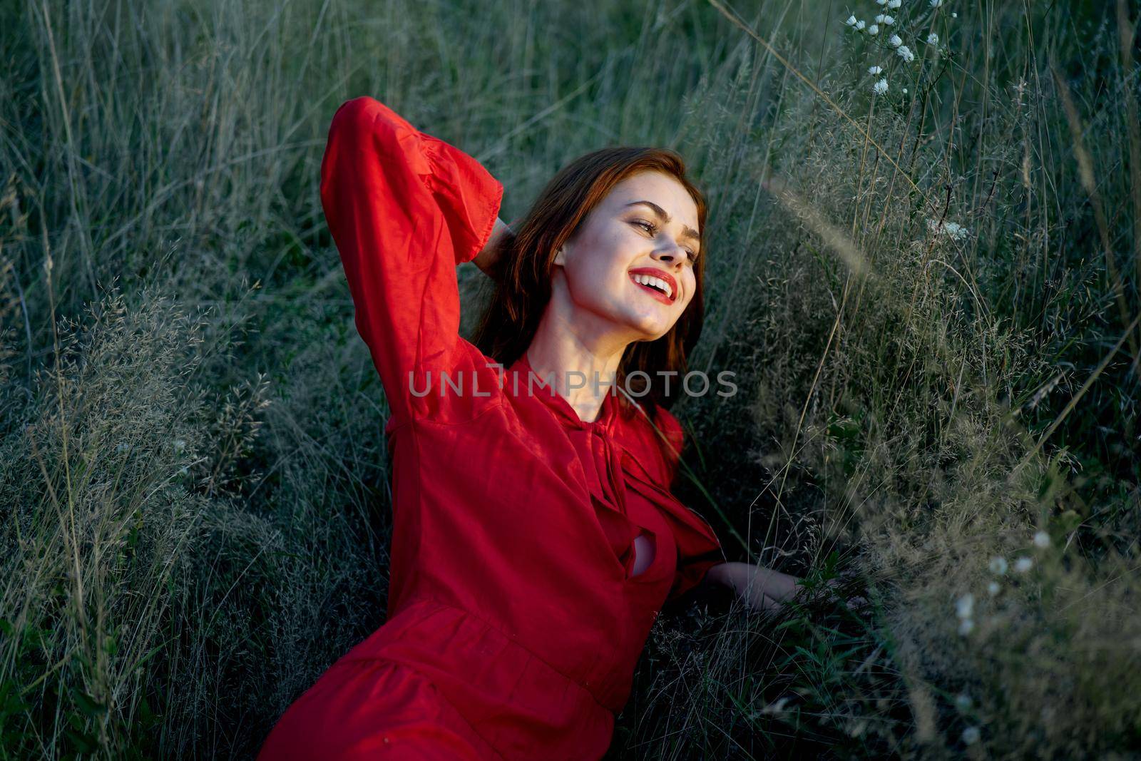 pretty woman in red dress lies on the grass nature sun. High quality photo