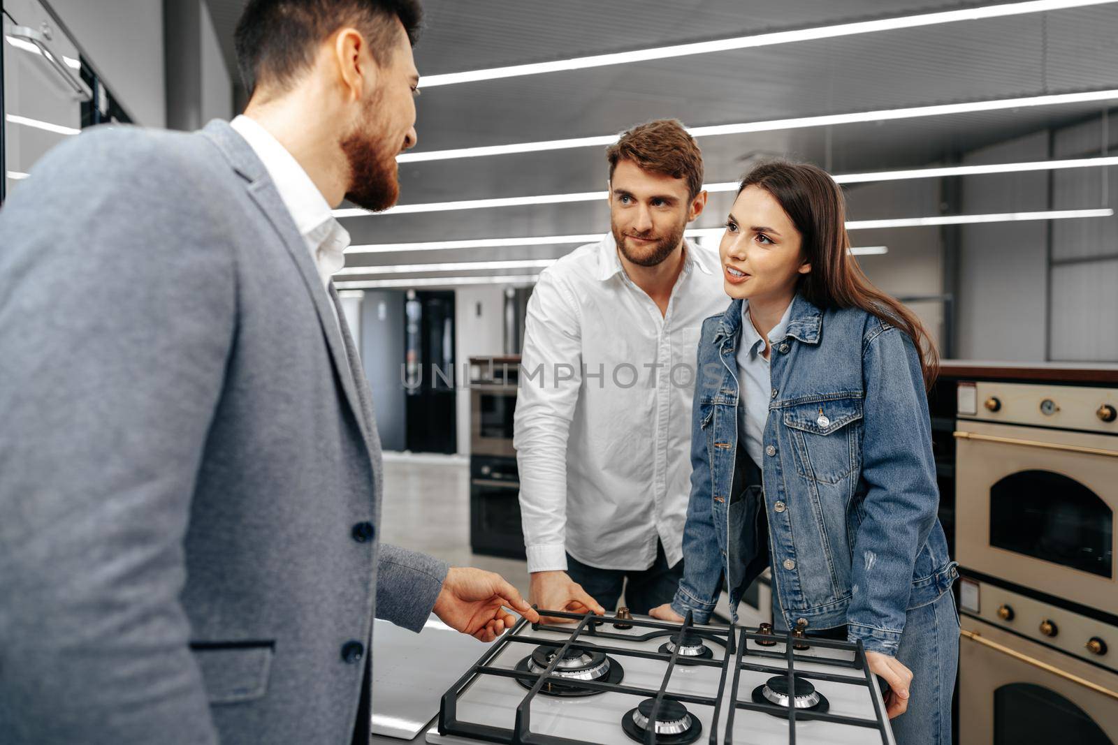 Male shop assistant helps young couple to choose new home appliance in hypermarket