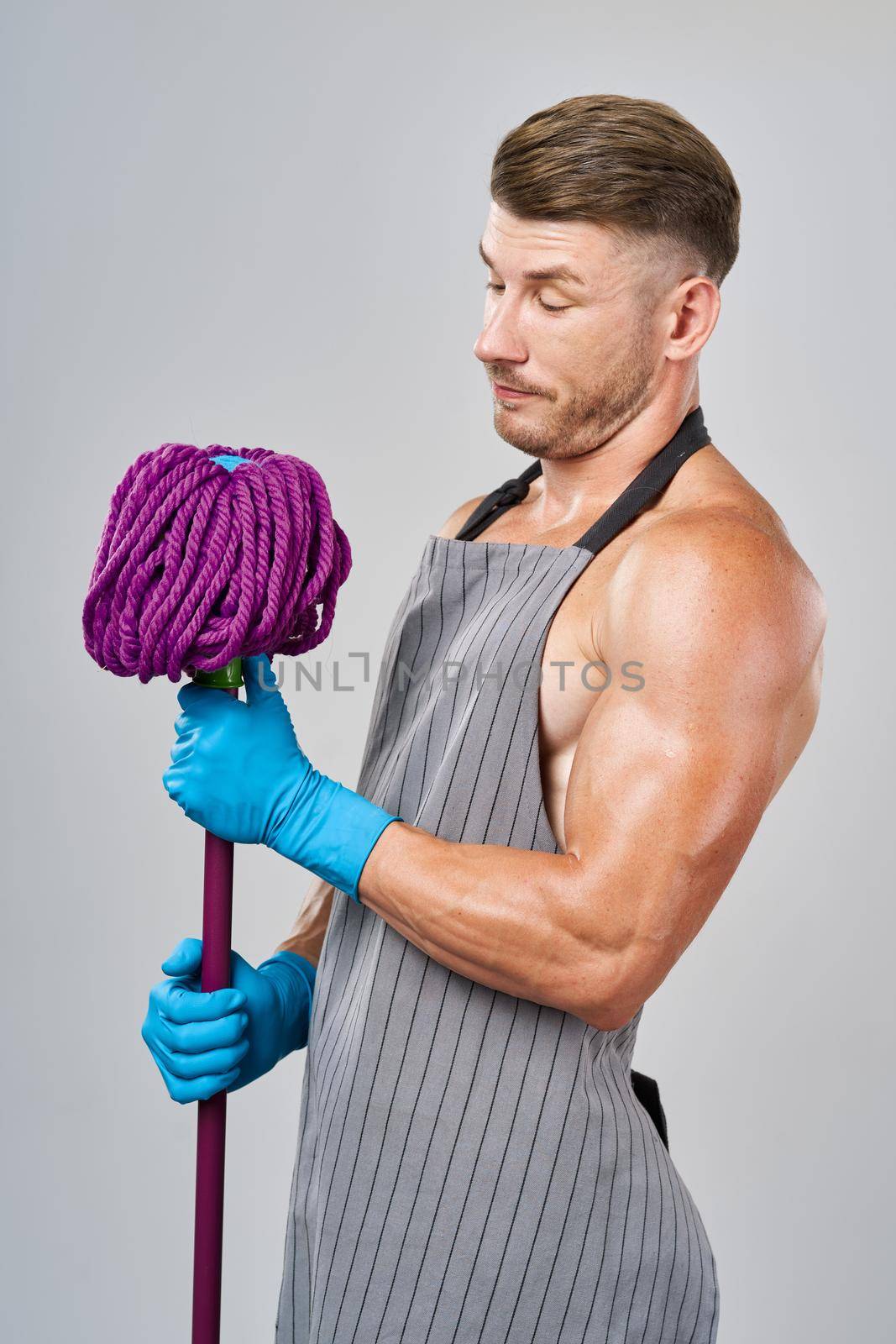 Muscled man in apron with mop posing cleaning. High quality photo