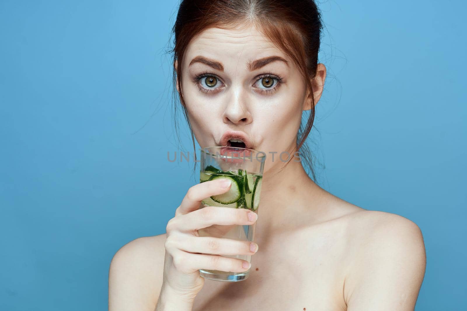 woman with bared shoulders cucumber health drink blue background. High quality photo