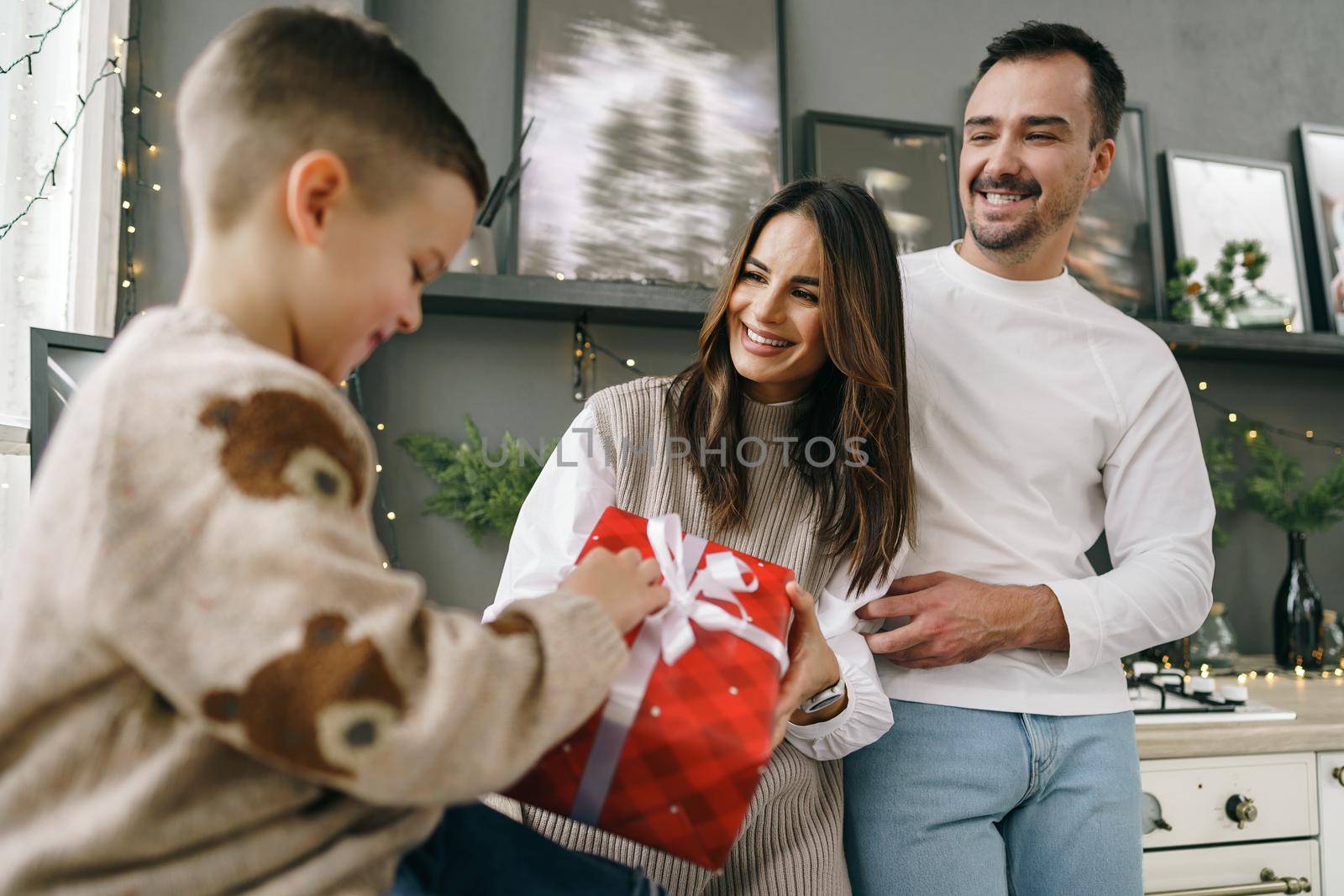 Smiling parents giving Christmas present to son at home by Fabrikasimf