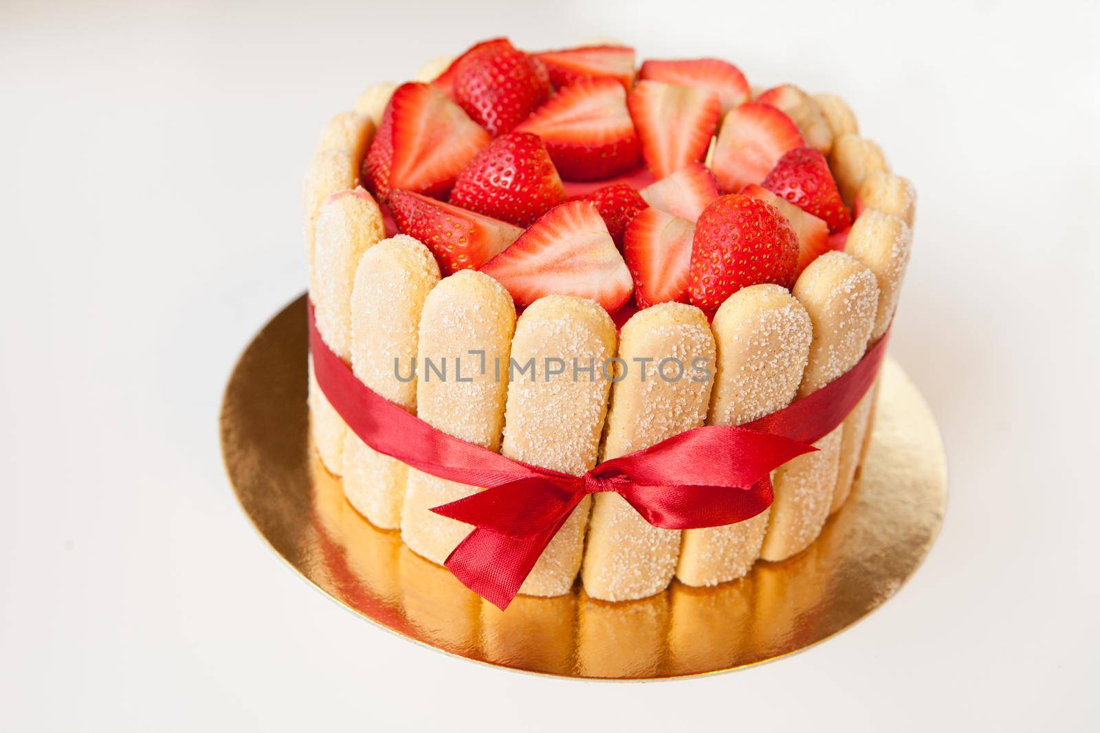 tiramisu cake with strawberries, ladyfingers, mascarpone and red bow-tape isolated on white. summer fruit charlotte cake on table