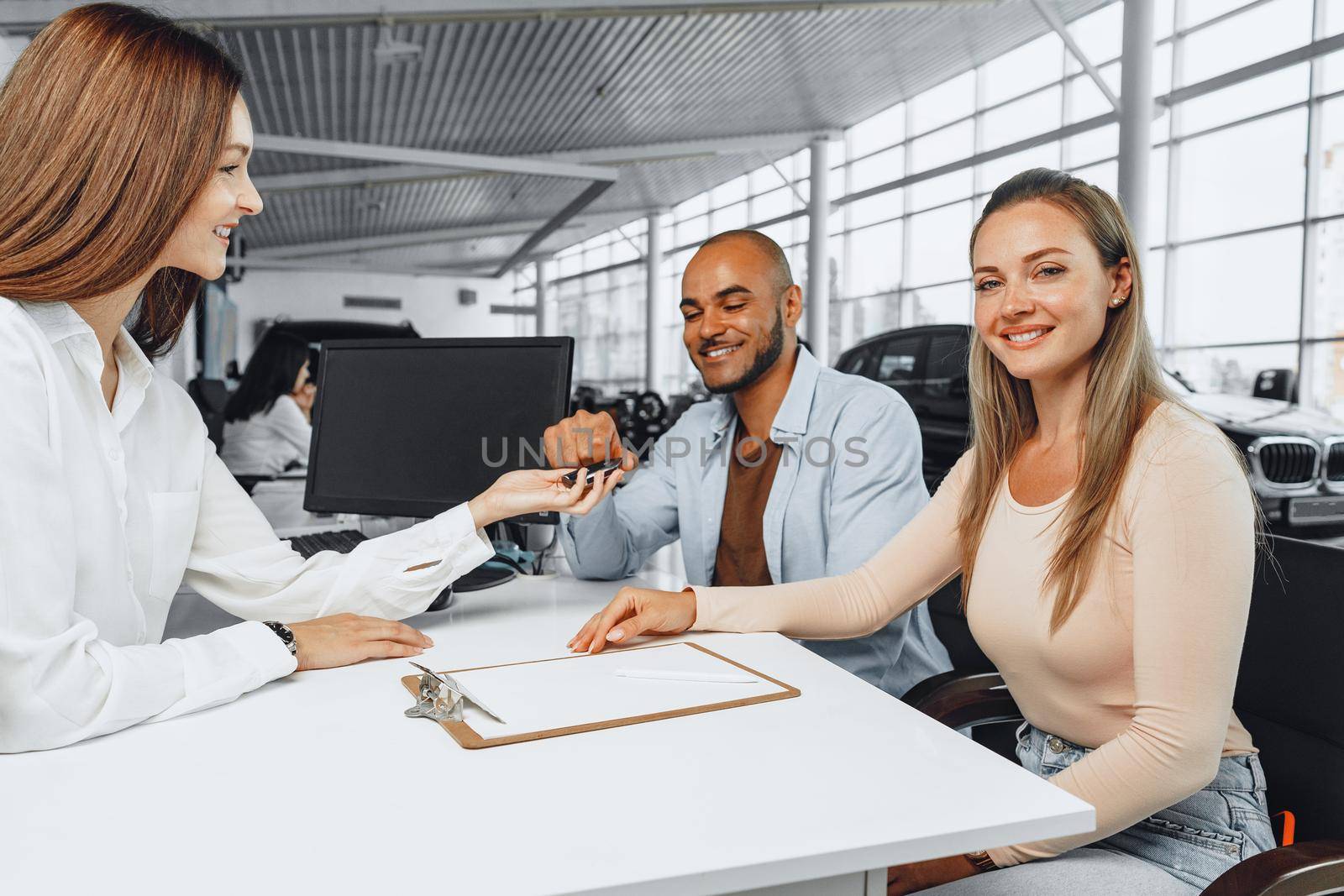 Cheerful couple taking keys of their new car in car dealership from saleswoman