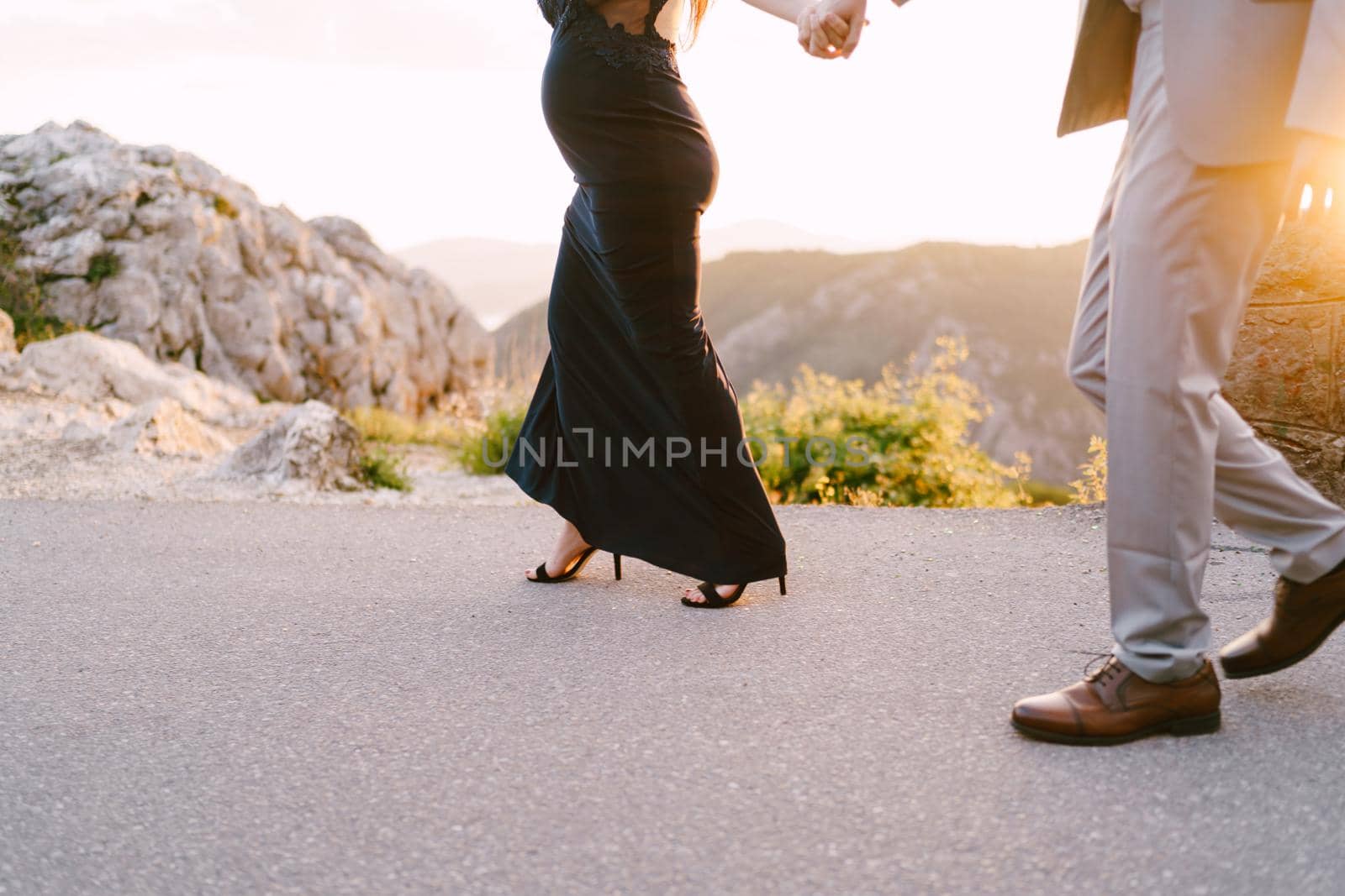 Man and a pregnant woman are walking along an asphalt road in the mountains. Close-up. High quality photo