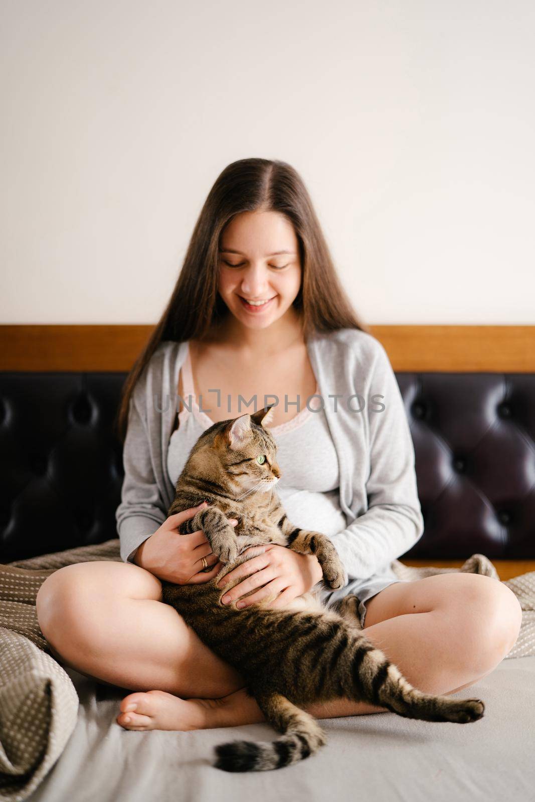 Pregnant woman sitting on bed with cat. High quality photo