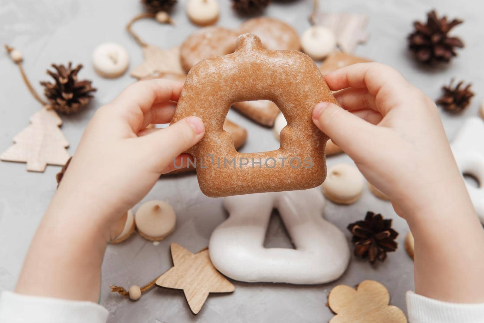 Children's hands hold a gingerbread in the shape of a home. The concept of Christmas sweets, toys, garlands and bokeh. Decor for New Year holidays.