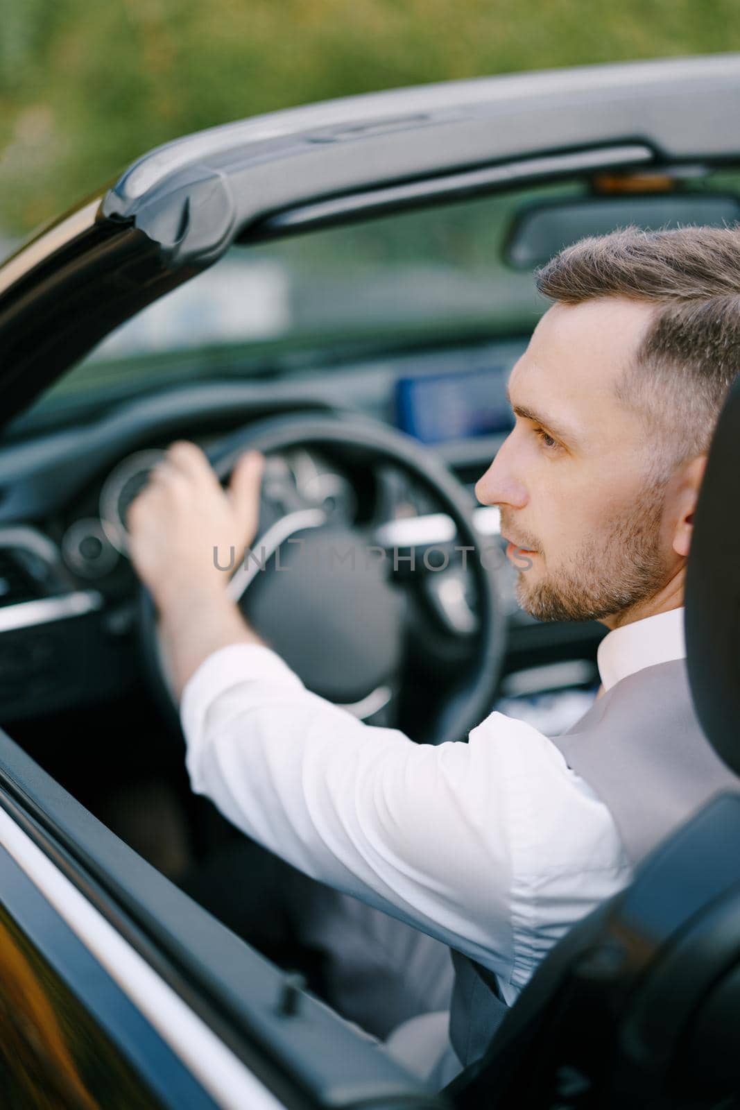 Man in a white shirt and vest sits at the wheel of a convertible. Back view. Close-up. High quality photo