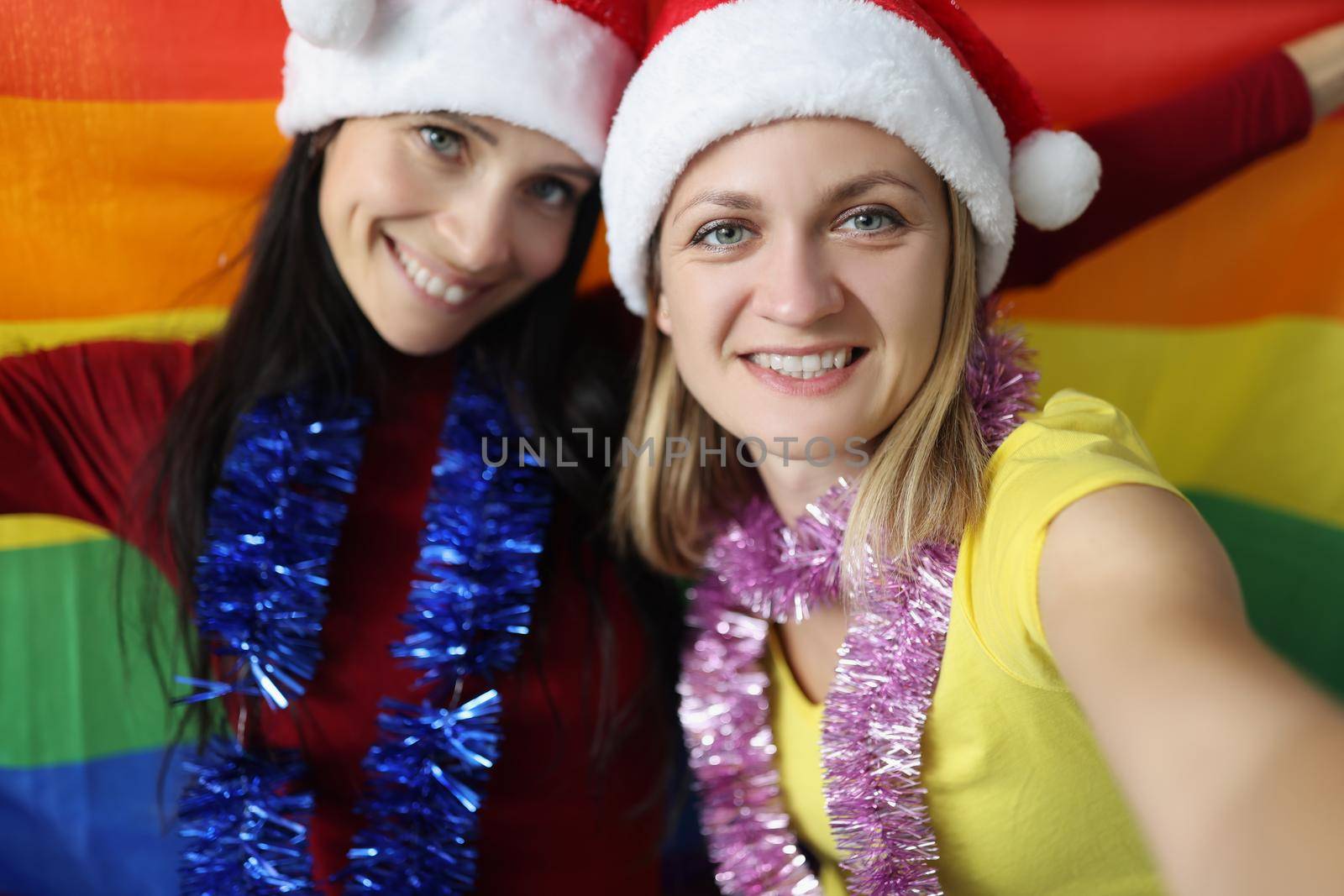 Portrait of female lovers happy about new year celebration hold lgbt flag. Smiling couple posing for picture. New year party, christmas, holiday concept
