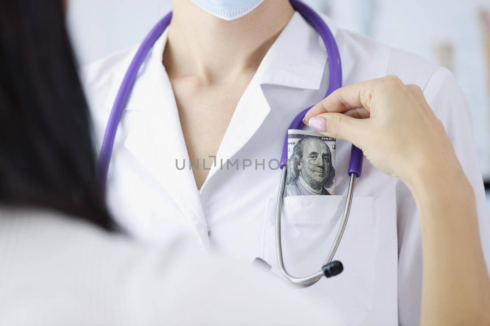 Close-up of woman patient put banknote in doctors pocket on appointment for better service. Pay to get qualified advice. Corruption in medicine concept