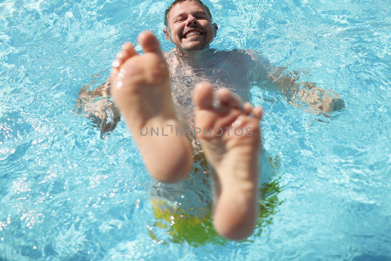Portrait of man diving into water in swimming pool with feet up. Laughing cheerful middle aged male enjoy summer hot water. Summertime, fun, chill concept