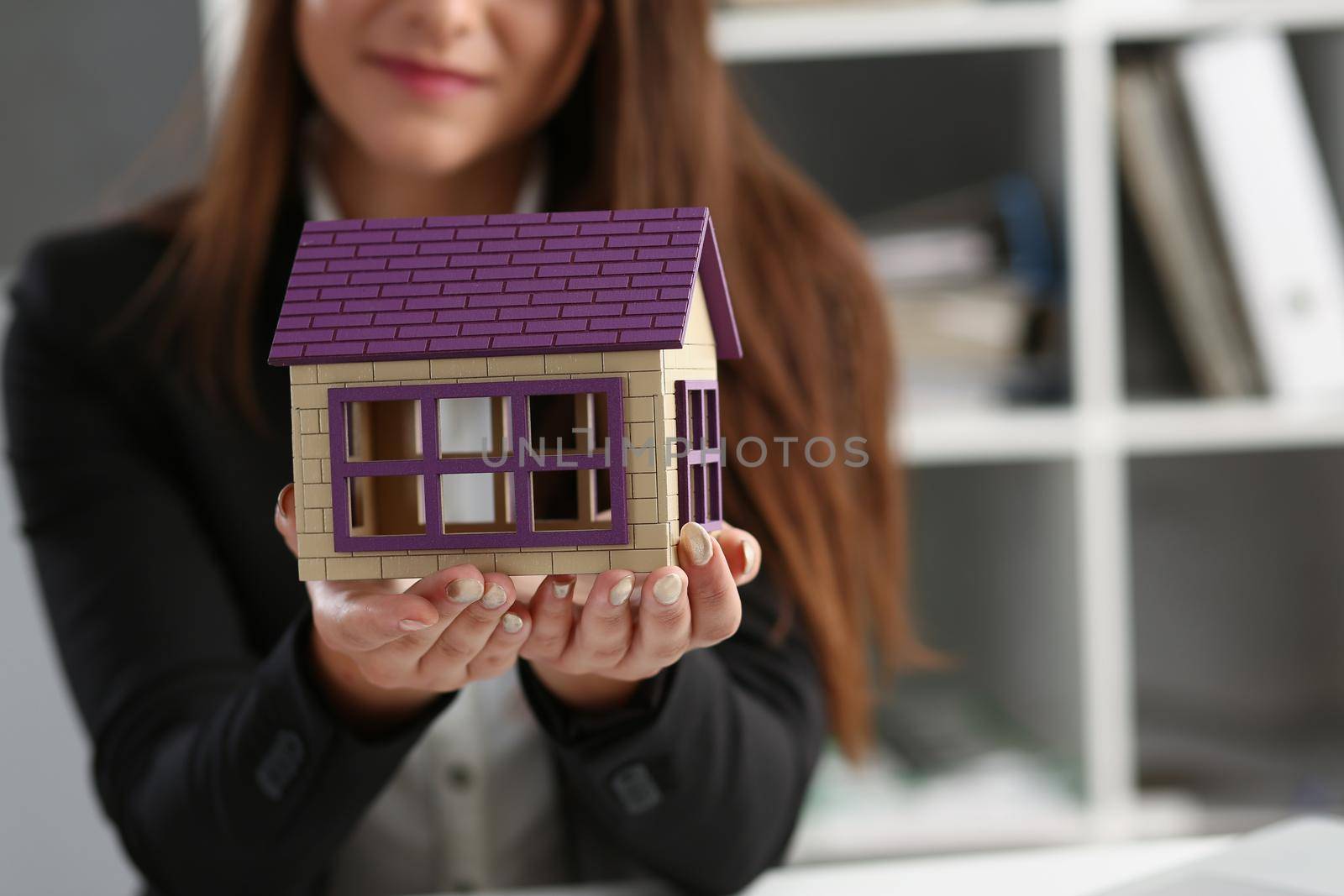 Close-up of woman in office hold miniature toy house in hand symbol of real estate. Sale or rent construction of apartment and housing for families concept