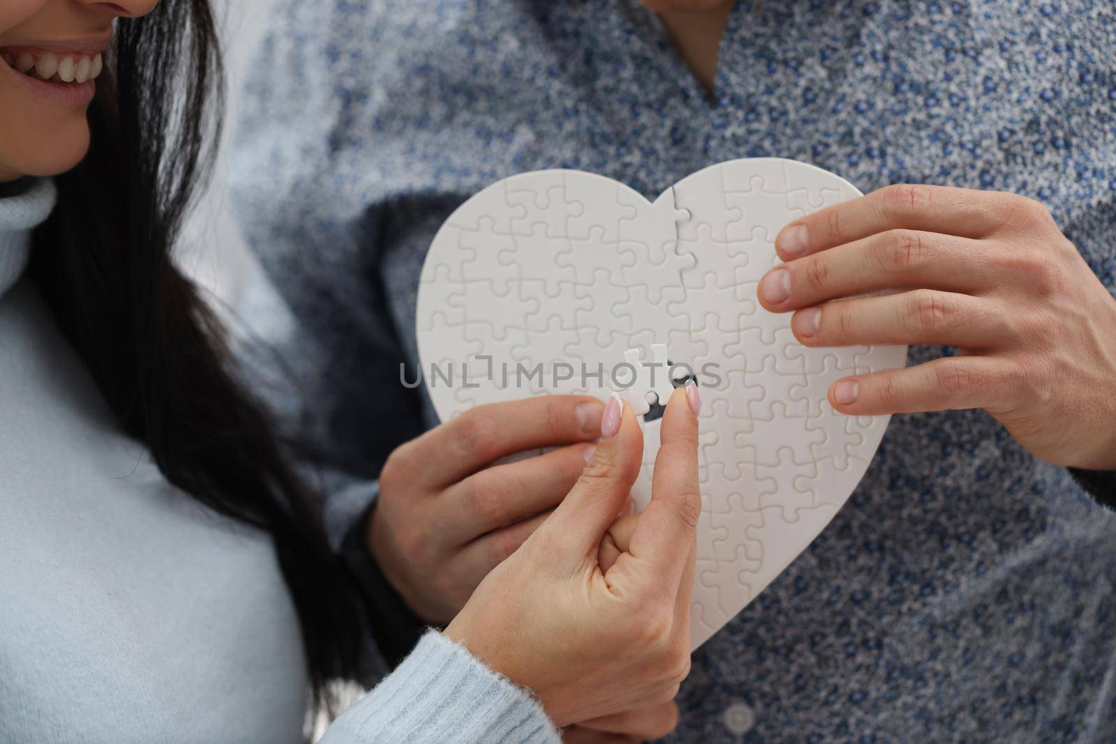 Close-up of woman and man fill empty space with missing piece of white heart puzzle. Find missing detail as symbol for healing broken heart. Love concept