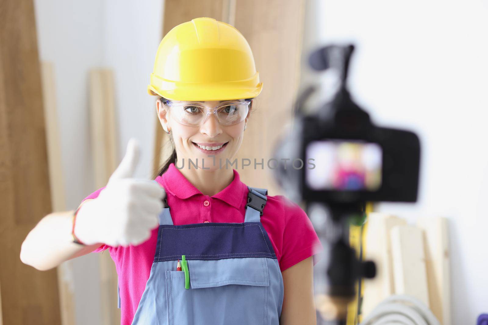 Portrait of happy woman construction site worker show thumbs up on camera. Film process on camera as educational lesson. Renovation, design, tech concept