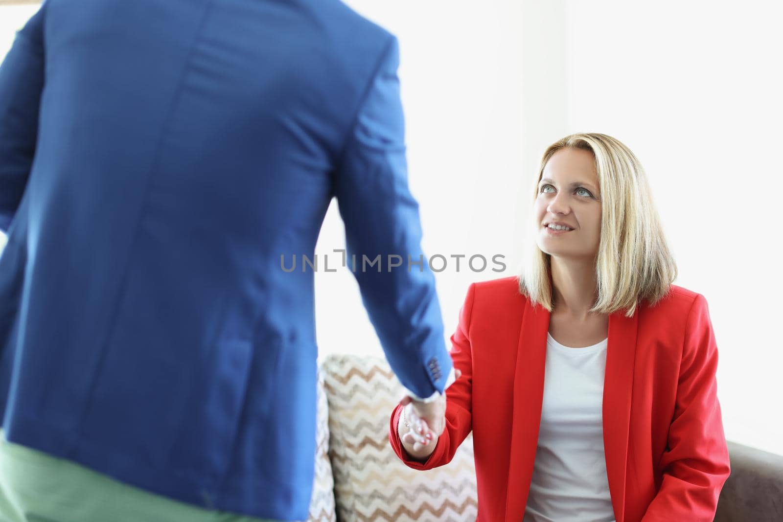 Portrait of attractive young female greeting man with handshake sitting on couch. Business meeting to sign up contract. Deal, agreement, success concept