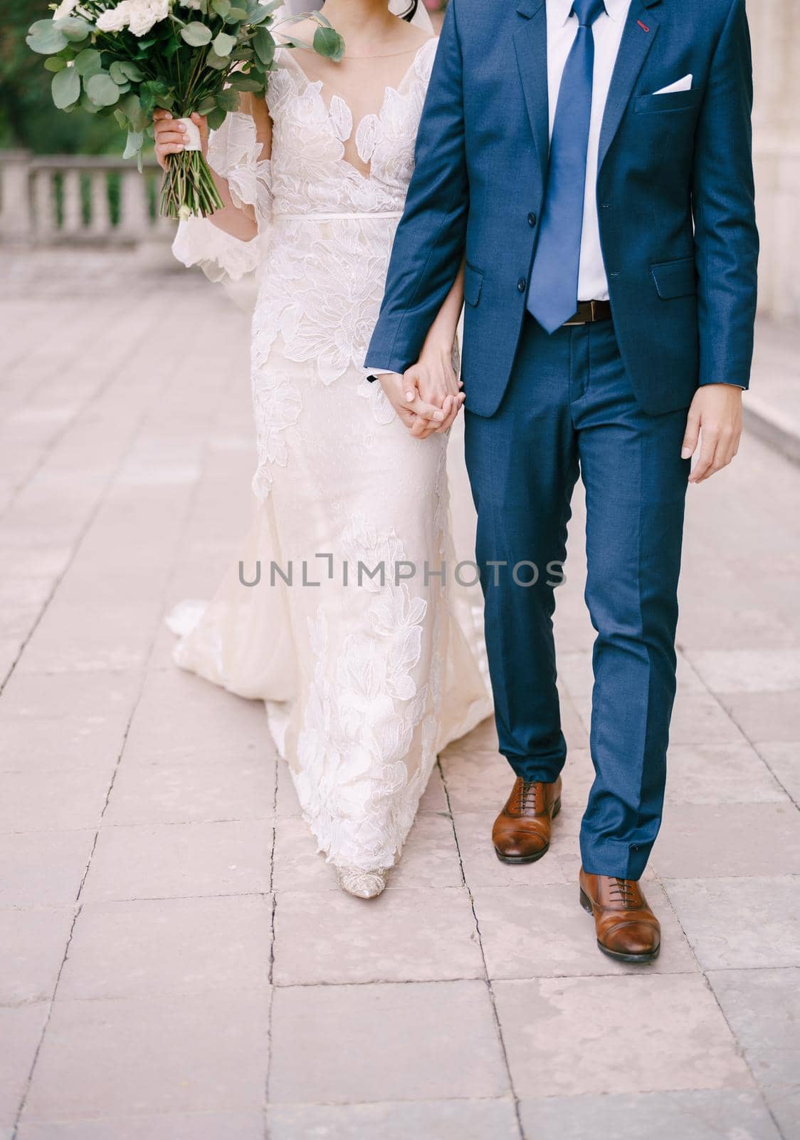 Bride and groom walk along the cobblestones holding hands. Close-up. High quality photo