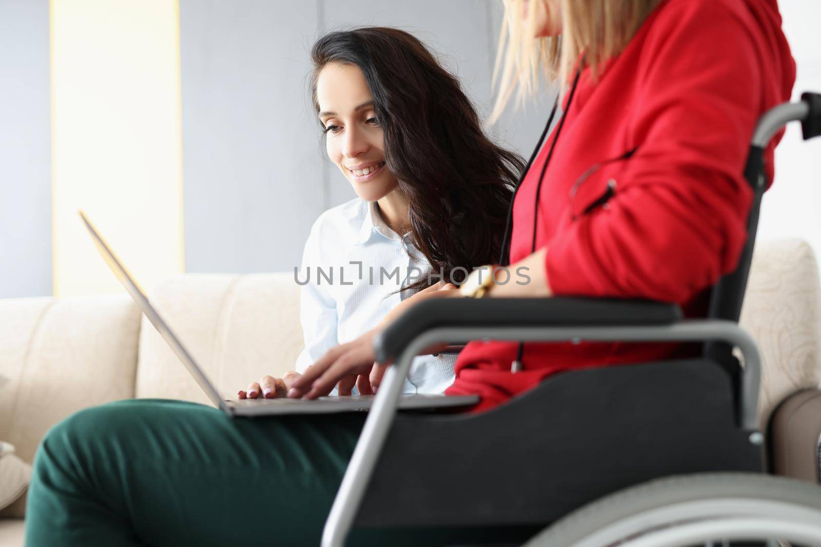 Best friends spend time together watching movie on laptop, woman in wheelchair hold device on lap by kuprevich