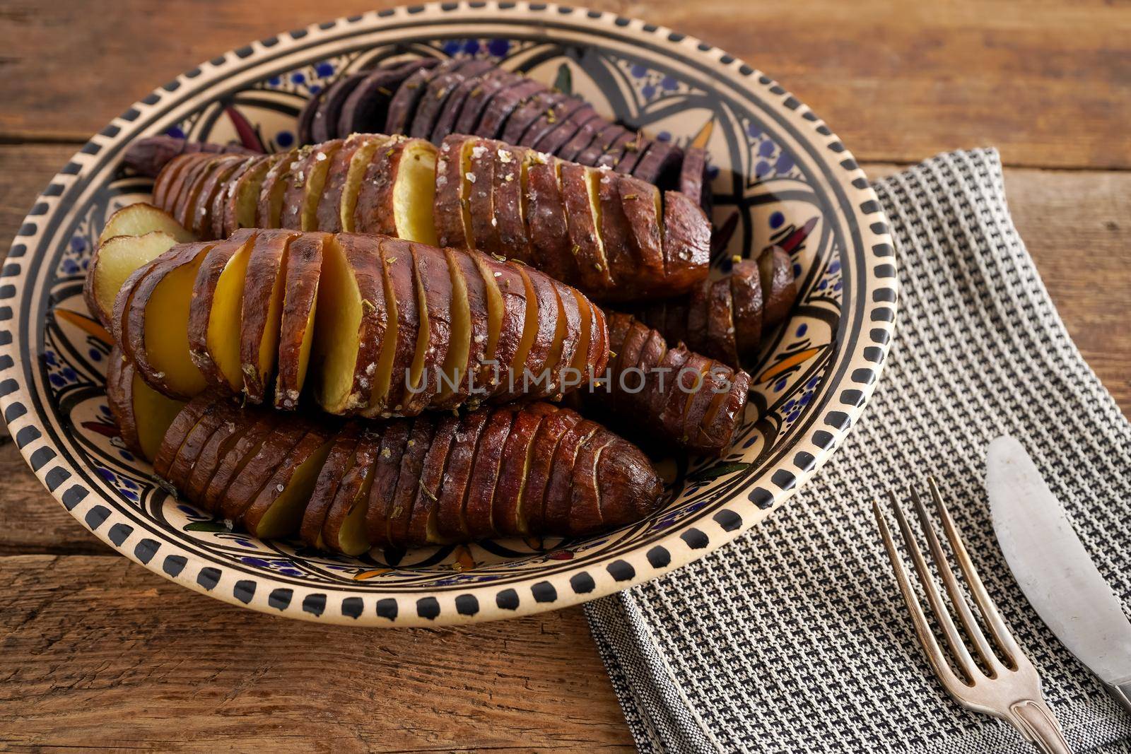 Sweet potato - sweet potatos tubers cooked in a pan. Fried and baked with spices and salt. Cut into pieces and slices. Healthy food close-up top view. Potato meal in a plate on a wooden table. Fork and knife.