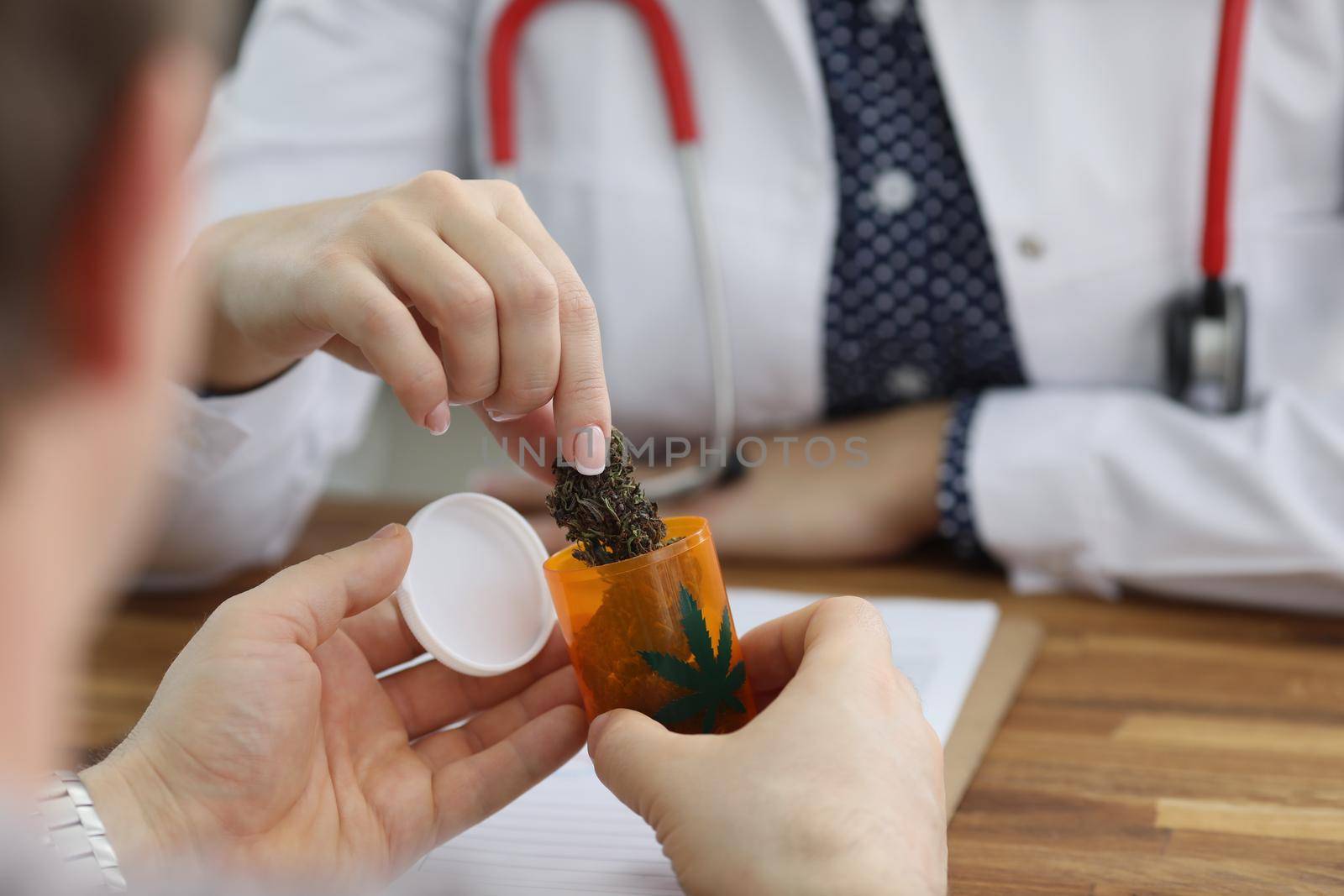 Close-up of doctor give bottle with dried cannabis to patient for health treatment. Man on appointment in hospital. Alternative medicine, health concept