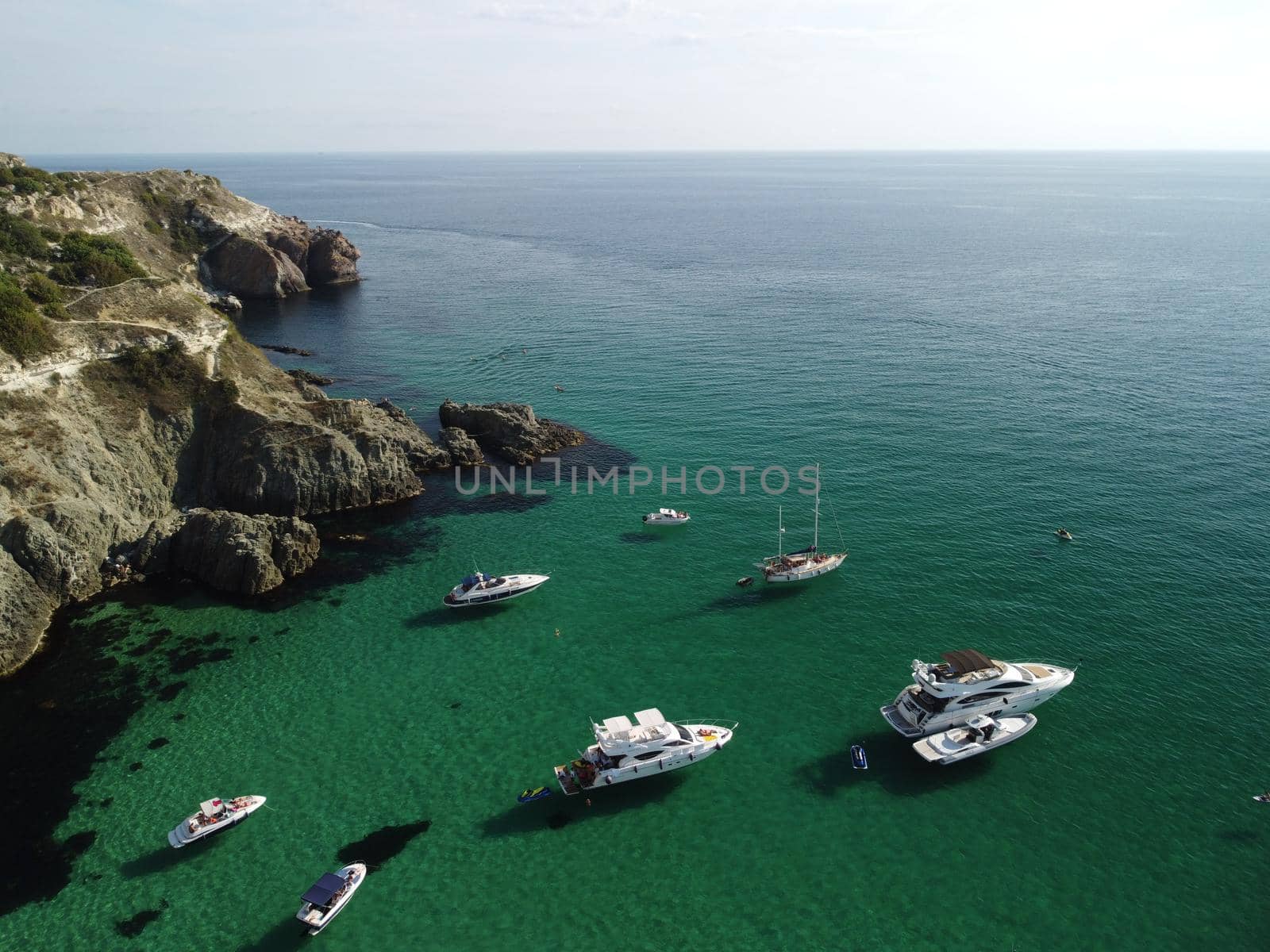 Sea landscape with rocky coastline on sunset time with cloudy sky. Yachts in the Sea on a background of rocky shores. The concept of perfect place for summer travel and rest.