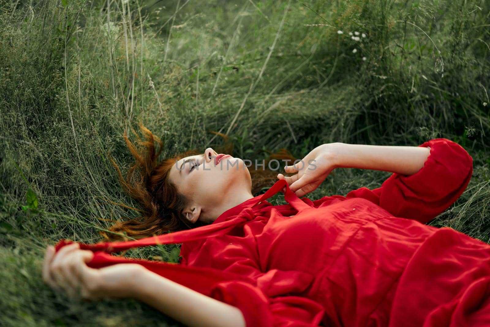 pretty woman in red dress lies on the grass in the field nature fresh air. High quality photo