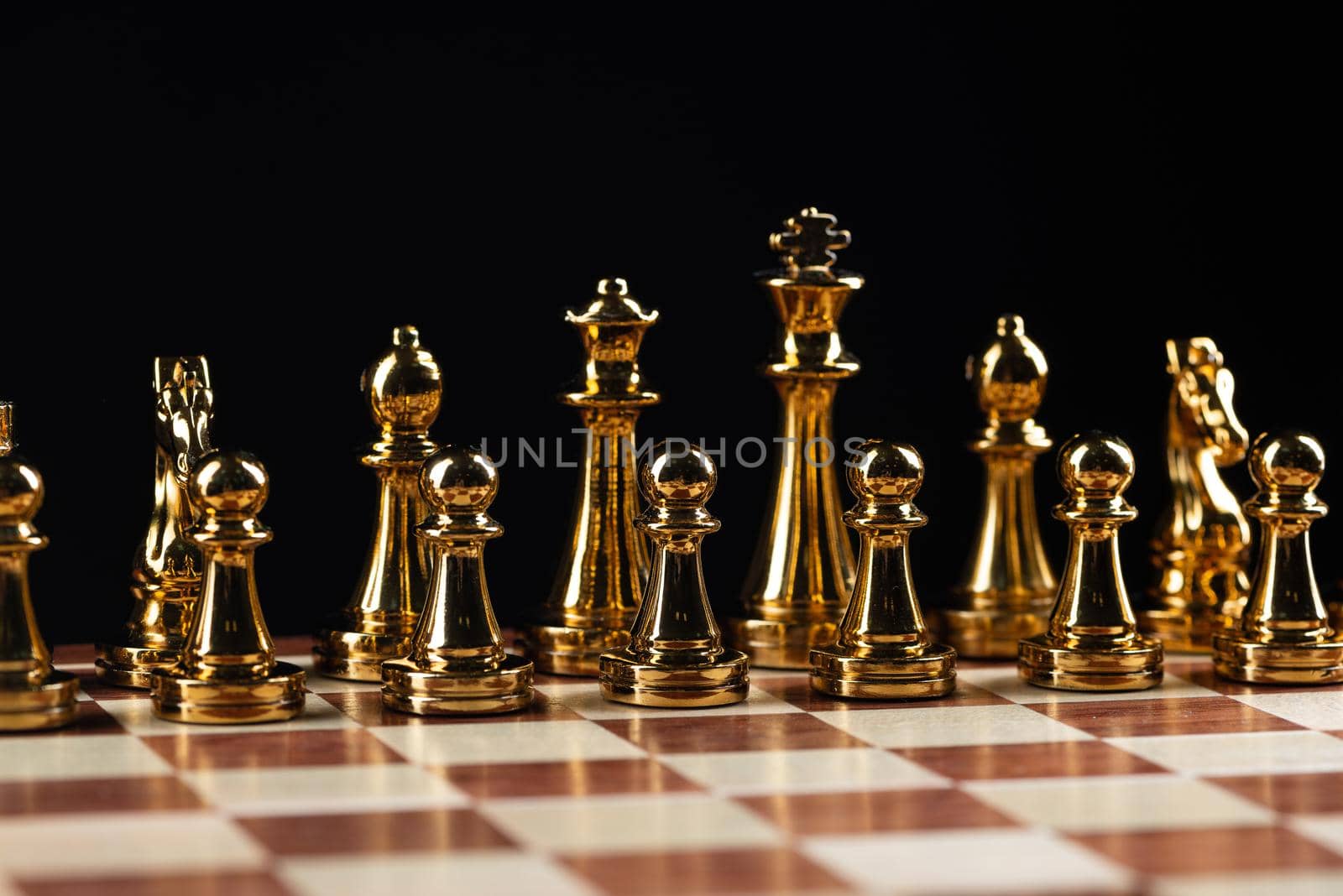 Golden chess figures standing on wooden chessboard. Intellectual duel and tactical battle in business. Strategy planning and leadership concept. Gold metal chess pieces in row on black background.