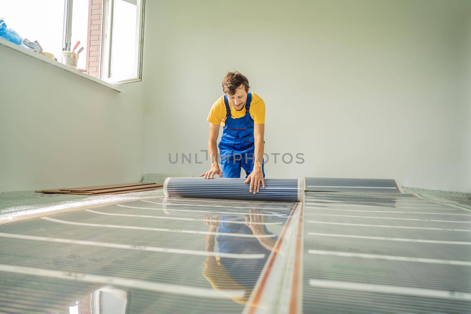 Master installs film warm floor in the room. Floor heating installation by galitskaya