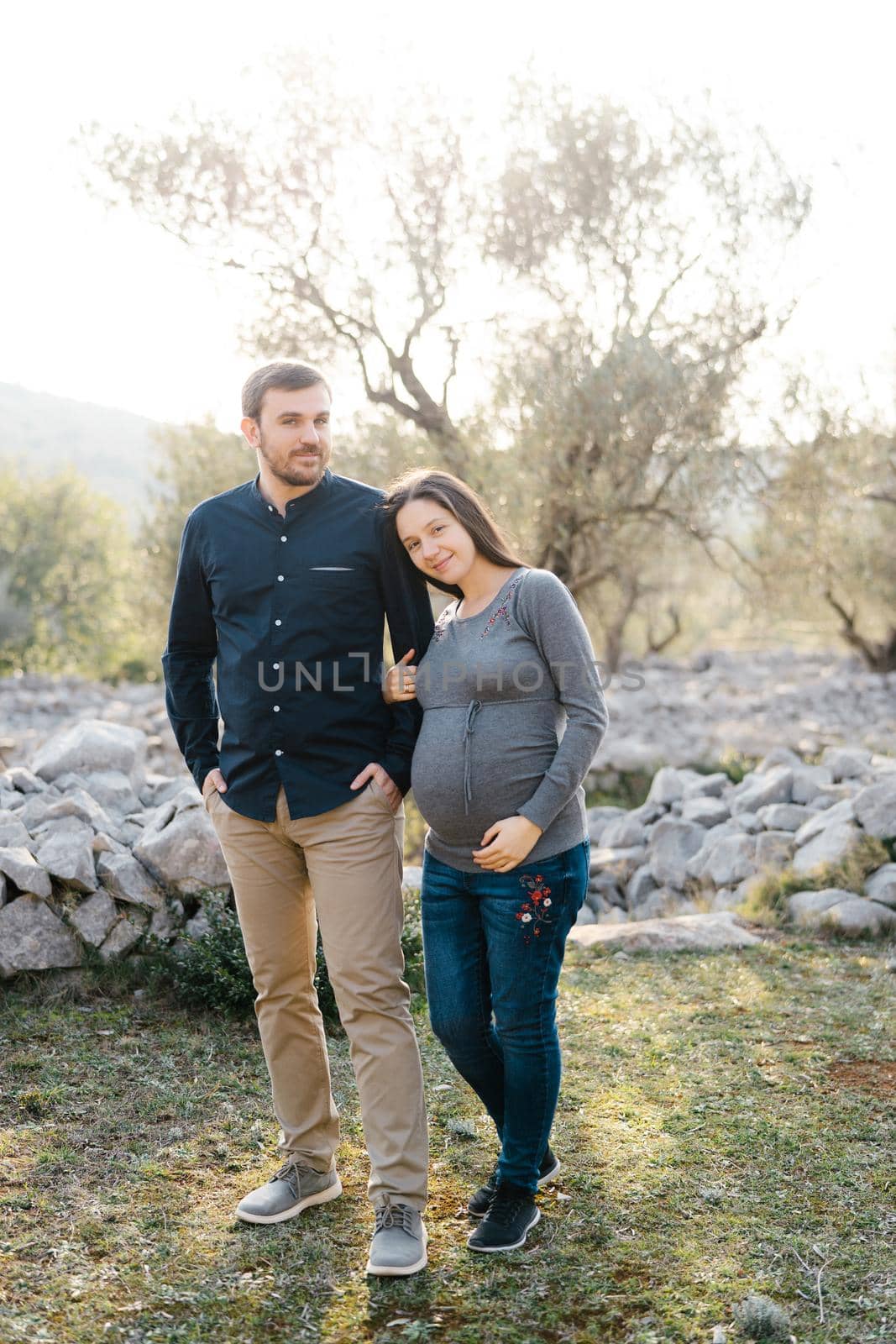 Smiling pregnant woman holding the arm of a man in a grove. High quality photo