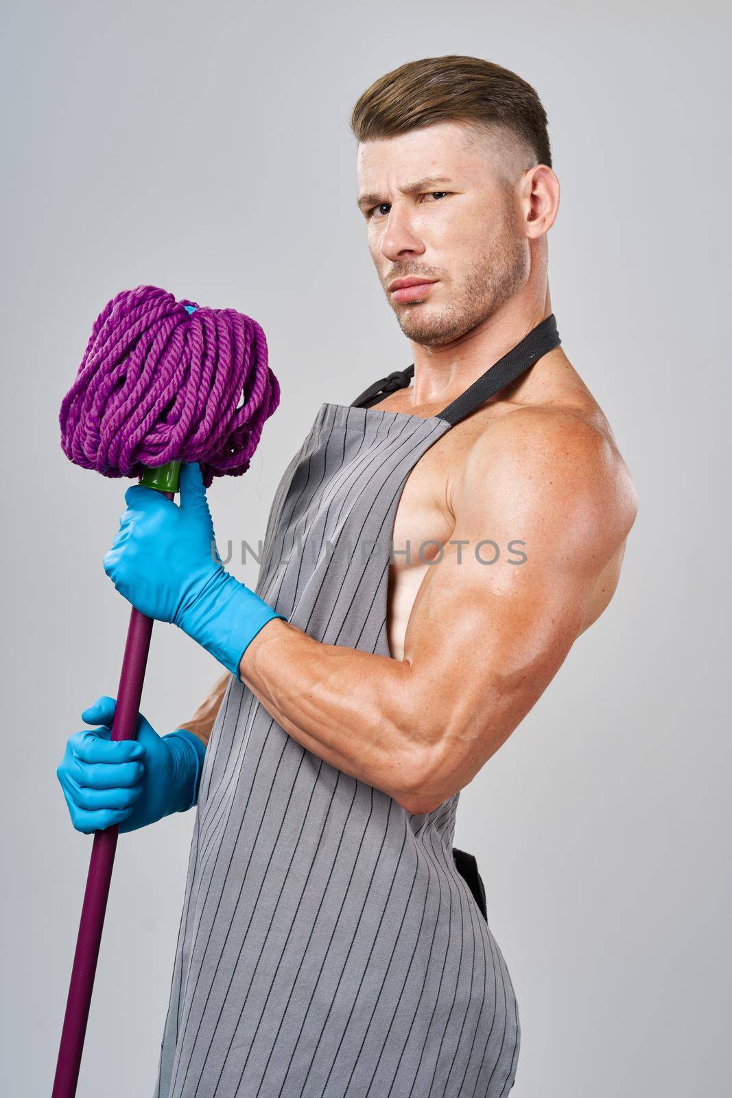 Muscled man in apron with mop posing cleaning. High quality photo