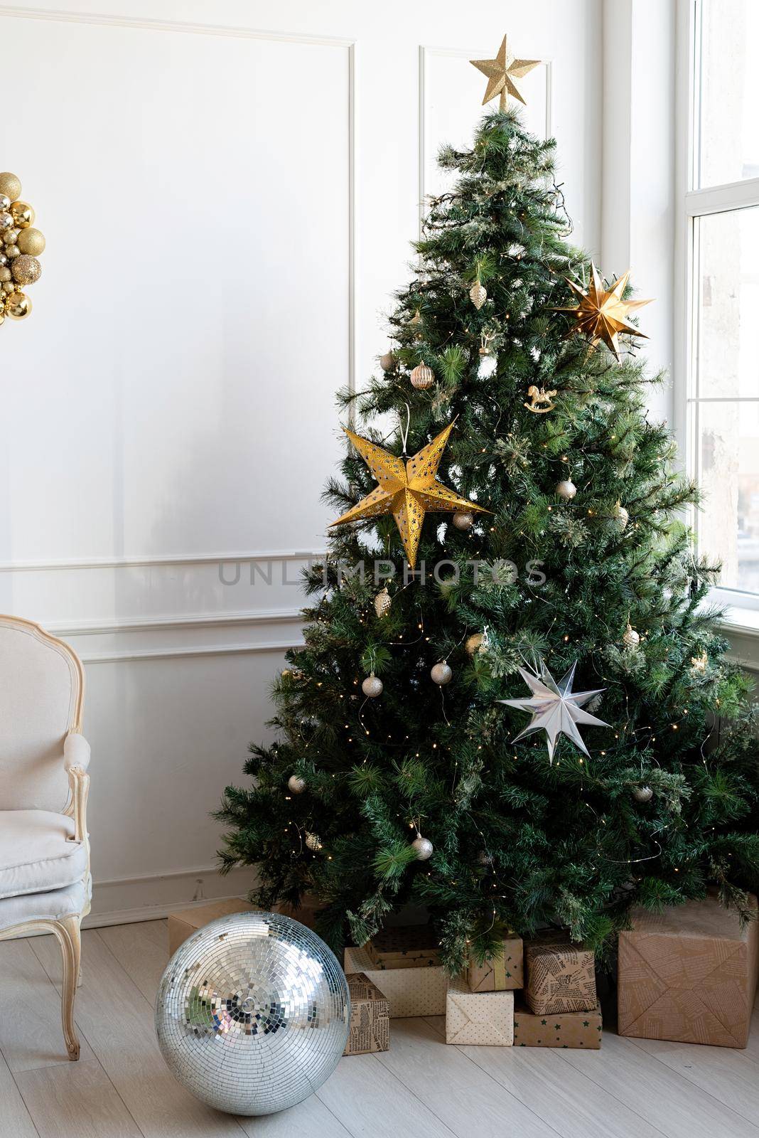 Merry Christmas and Happy New Year. Christmas tree with presents and lights in light and airy living room next to the window