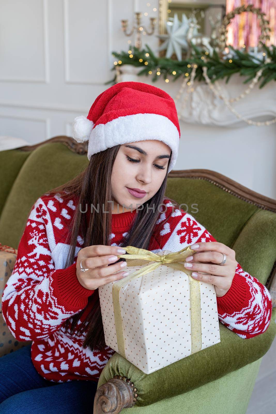 Packaging holiday gifts. Christmas gift wrapping. Young woman in red sweater wrapping a gift sitting on the couch