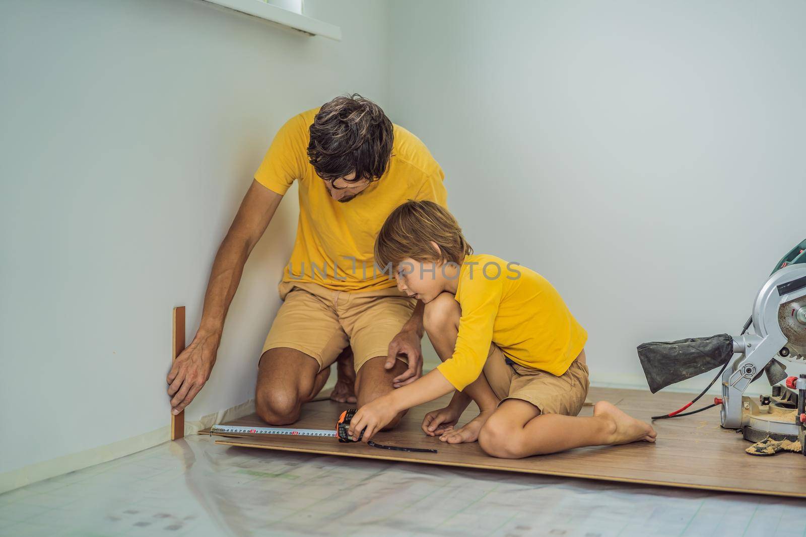 Father and son installing new wooden laminate flooring on a warm film floor. Infrared floor heating system under laminate floor by galitskaya