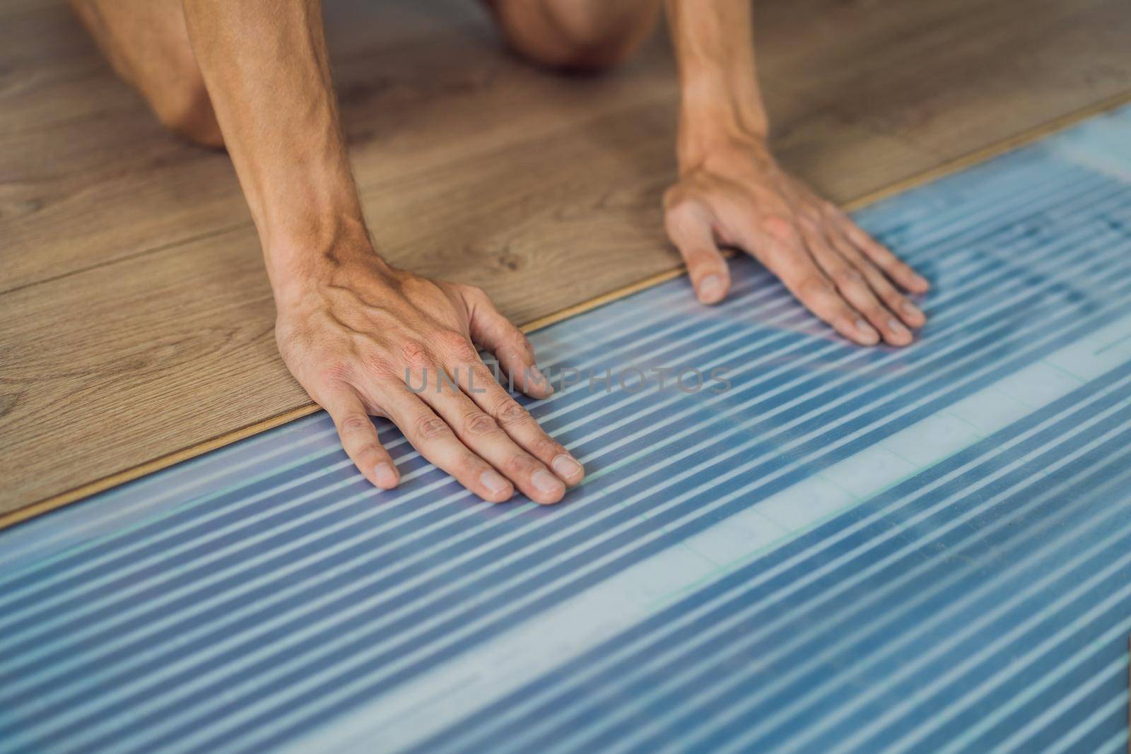 Man installing new wooden laminate flooring on a warm film floor. Infrared floor heating system under laminate floor by galitskaya