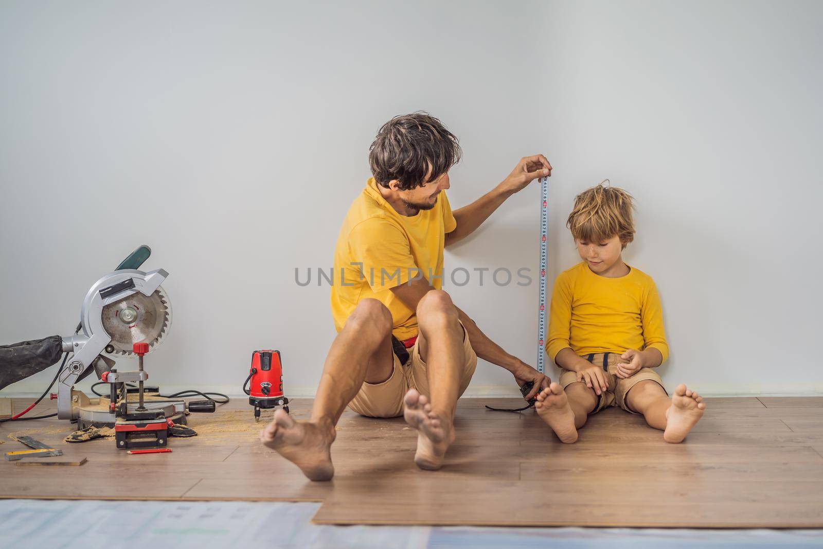 Father and son installing new wooden laminate flooring on a warm film floor. Infrared floor heating system under laminate floor.