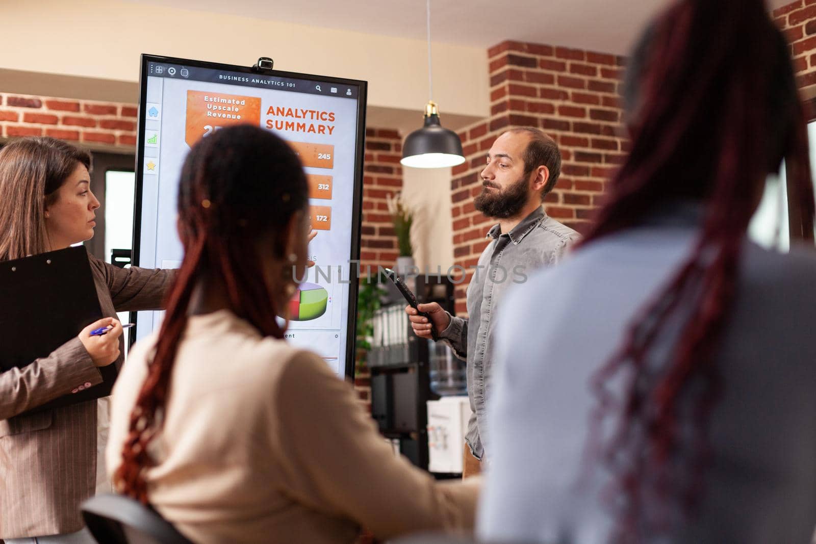 Businessman pointing at monitor explaining marketing statistics to businessteam working at company presentation in startup office. Diverse businesspeople planning business presentation
