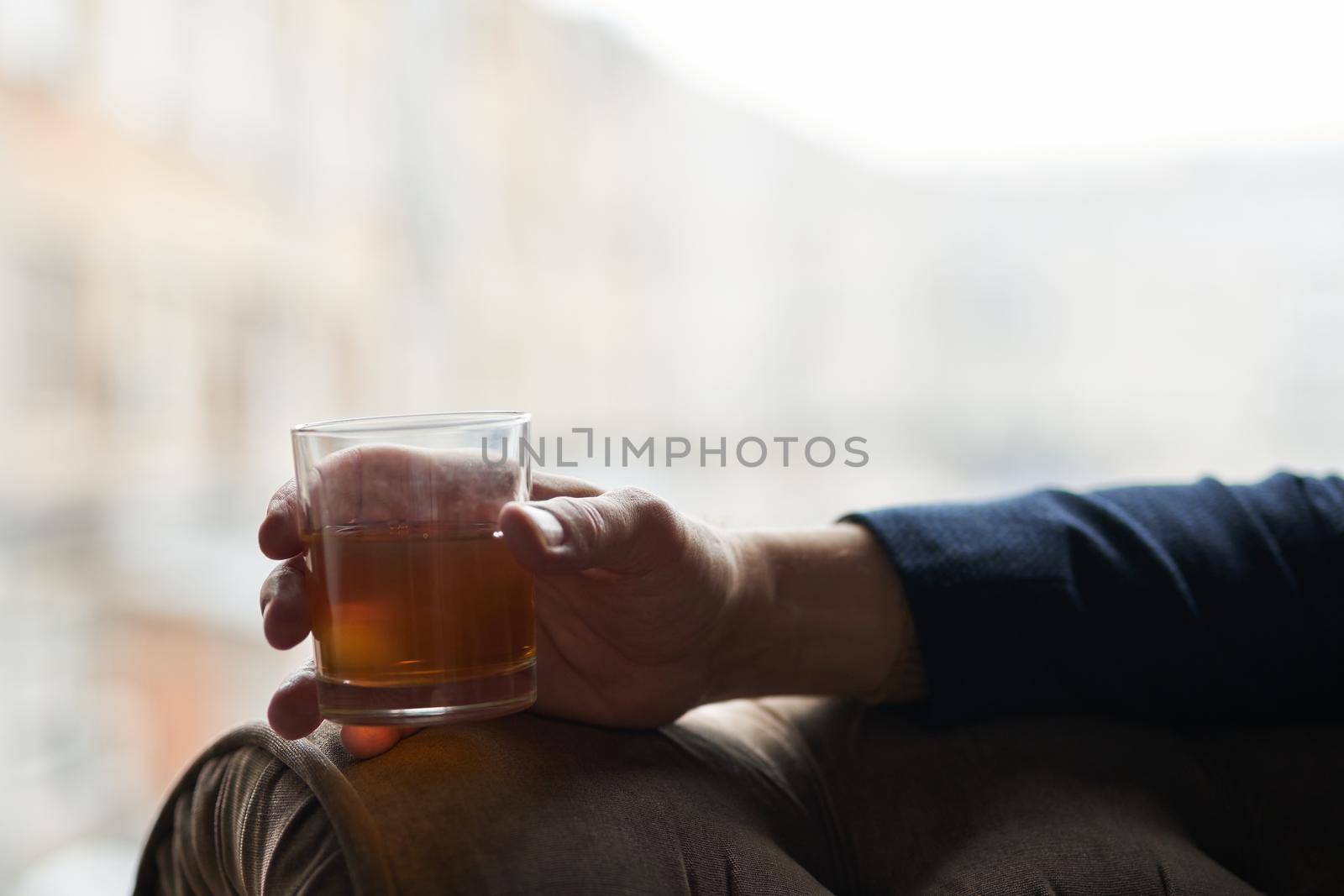 Close up shot of hand of successful business man holding glass of alcohol scotch whiskey while relaxing in a chair. Lifestyle, success, people concept