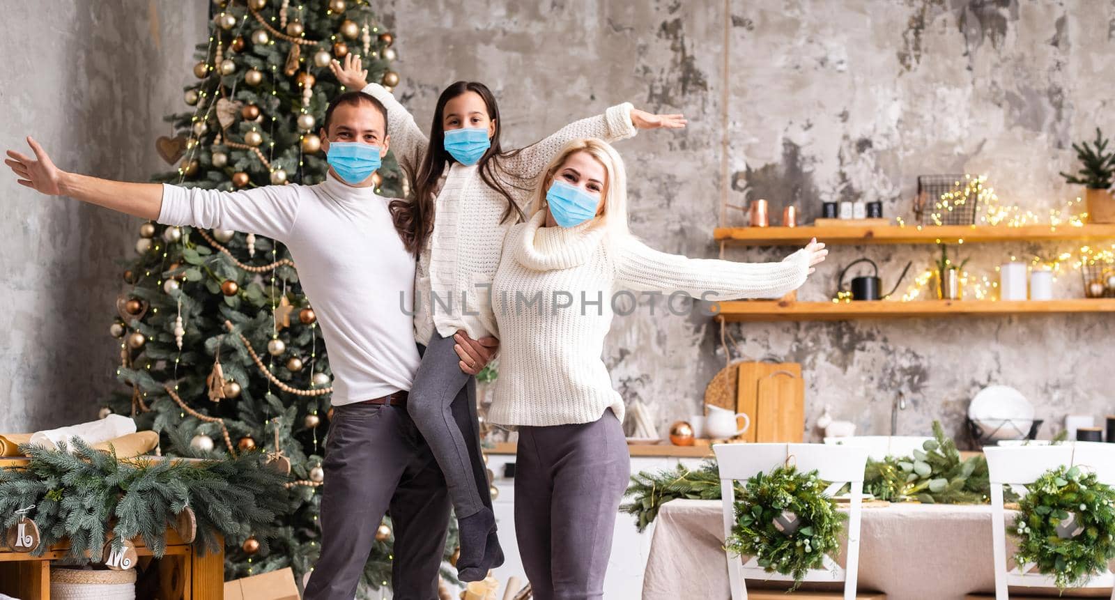 A happy family wear medical masks due to the COVID-19 coronavirus near Christmas tree. Xmas holidays.