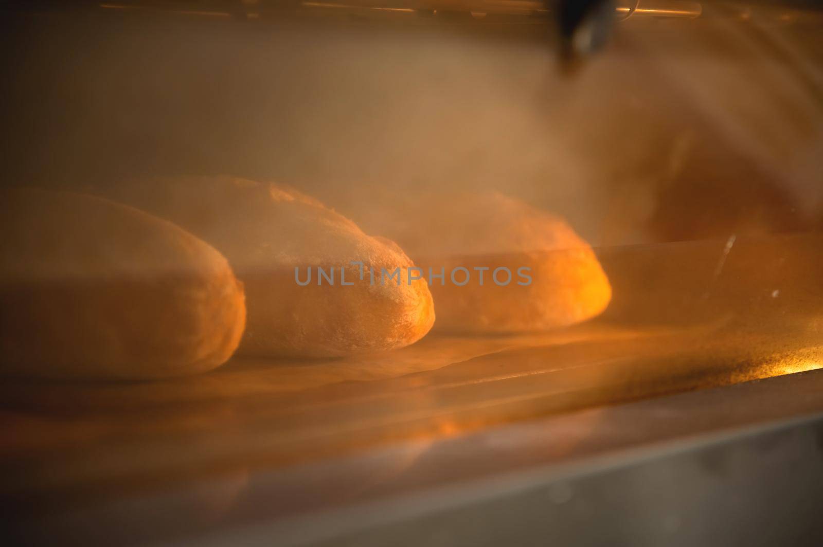 Batch of fresh buns baking in an oven viewed through the glass door with reflections in a cooking and food concept.