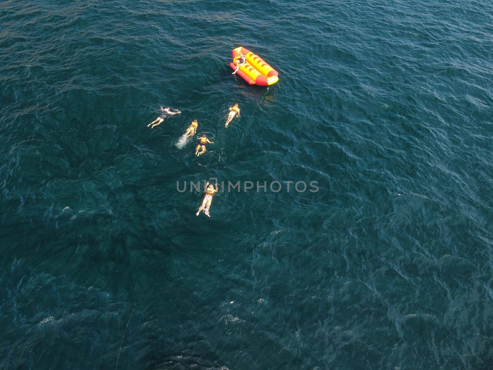 Happy people swim on air mattress behind a high speed water bike. Tourists ride on inflatable watercraft boat. Sea attraction. Water boat skating people on large Inflatable raft. Aerial copter view