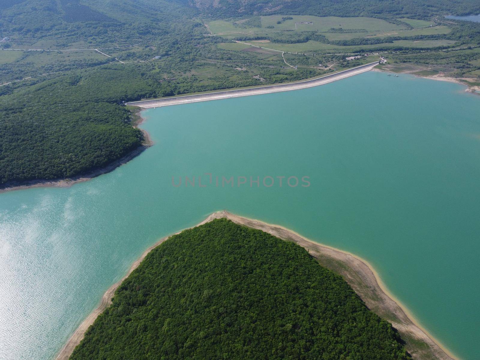 Aerial landscape from flying drone storage reservoir at mountain foot covered colorful autumn forest. Beautiful view from above blue lake among highlands
