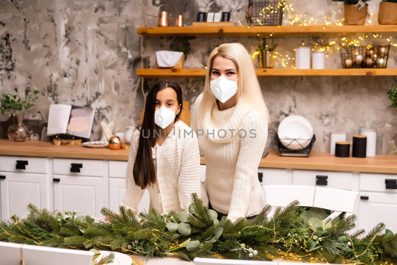 Beautiful mother and daughter in medical masks have fun at home near the Christmas tree in a interior. Family happiness, holiday, joy, vacation, games with a woman. New Year's preparations by Andelov13