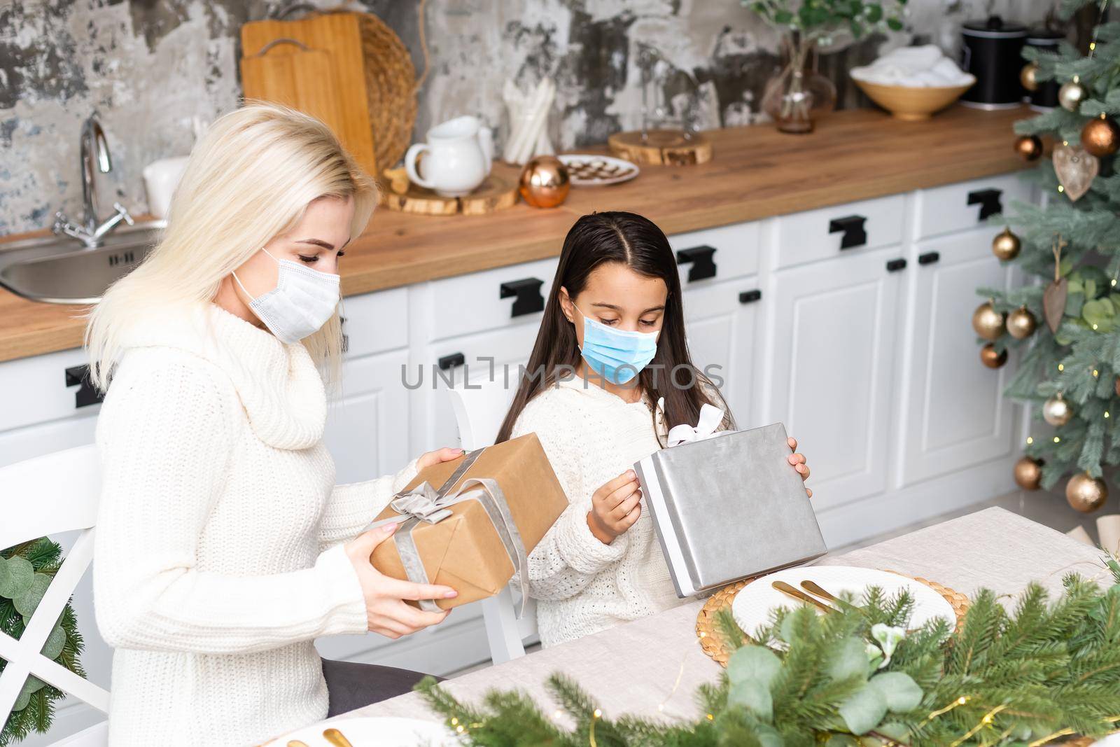 Beautiful mother and daughter in medical masks have fun at home near the Christmas tree in a interior. Family happiness, holiday, joy, vacation, games with a woman. New Year's preparations by Andelov13