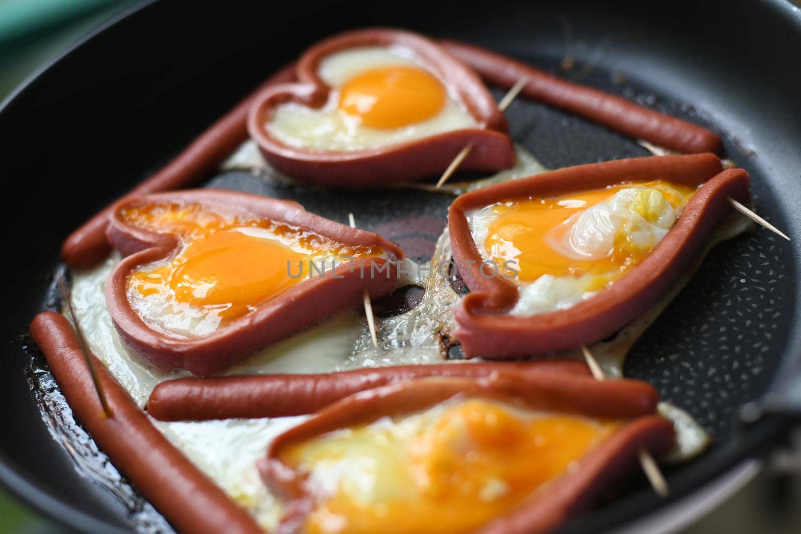 Heart-shaped fried eggs in sausages in a frying pan