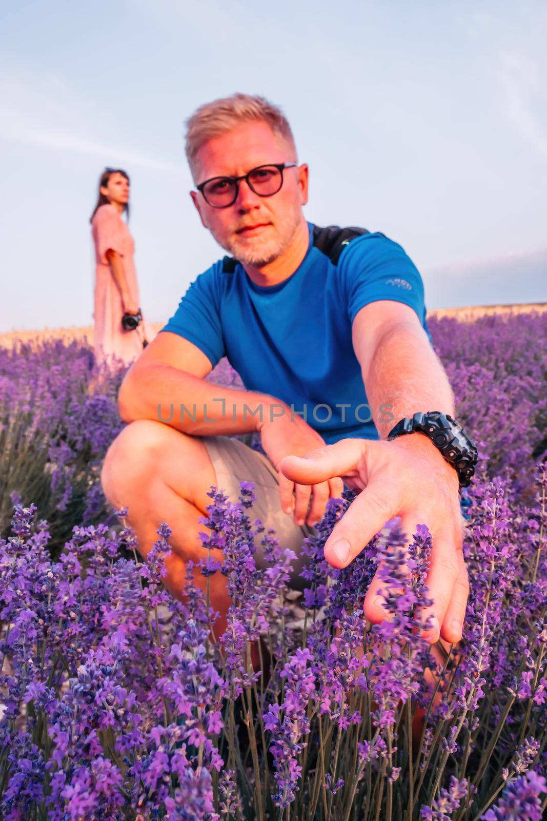 Close up portrait of happy young man in blue t-shirt and glasses on blooming lavender fields with endless rows. Warm sunset light. Bushes of lavender purple aromatic flowers on lavender fields by panophotograph